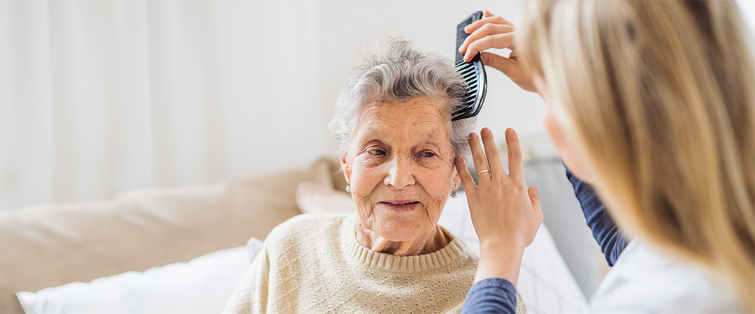 Caretaker gently combing an elderly woman's hair